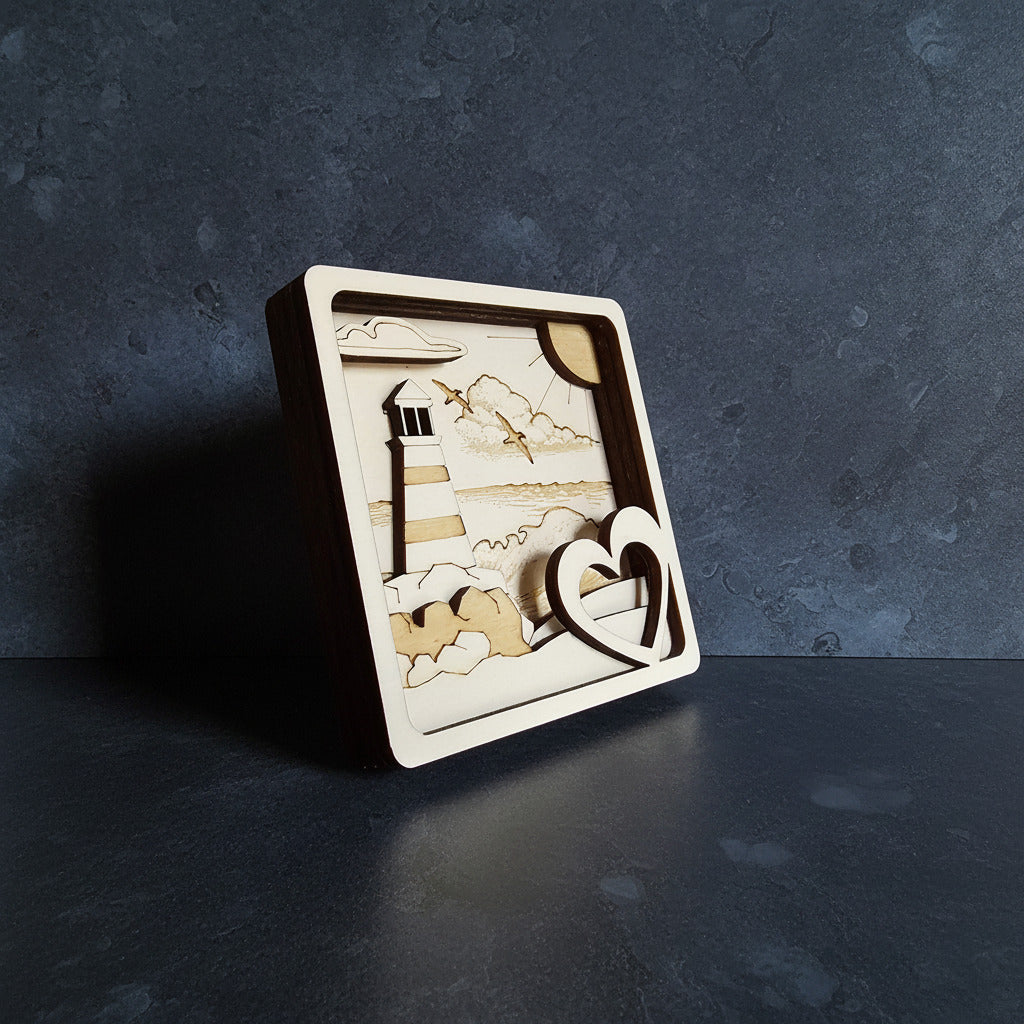 3D Multilayer-Bild Leuchtturm mit Herz aus Sperrholz, lasergraviert, Schrägansicht mit dunklem Rahmen auf grauem Untergrund